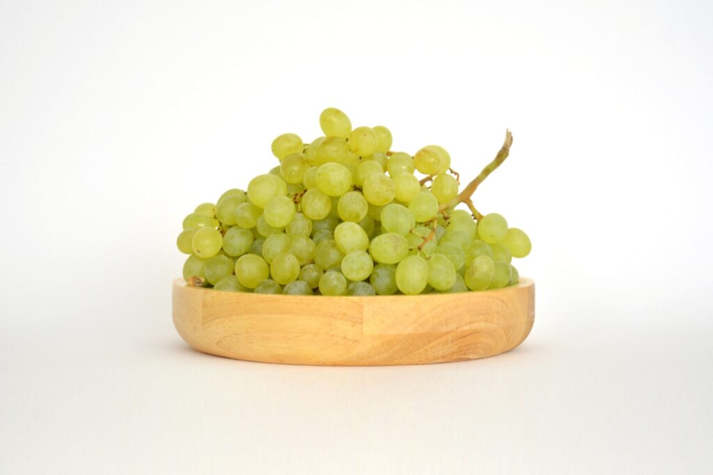A wooden bowl filled with green grapes